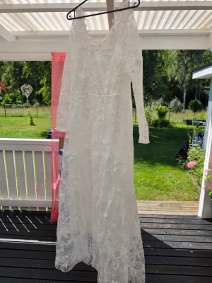 Ny lång brudklänning stl XL - Säljer en elegant vit långklänning med vackra spetsdetaljer och långärmad design. Klänningen har en romantisk känsla med transparenta ärmar och blommigt spetsmönster. Perfekt för speciella tillfällen när du vill känna dig extra fin. Köptes som en extra brudklänning tidigt förra året innan jag visste vad jag ville ha. Endast provad 2 gånger. 