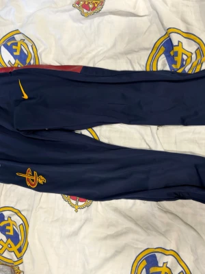Mörkblå träningsbyxor Nike - Säljer ett par mörkblå träningsbyxor från Nike med gul logga och detaljer. Byxorna har smal passform och är tillverkade i ett lätt och stretchigt material, perfekta för sport eller träning.