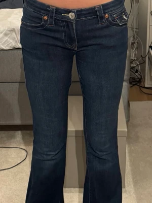 Mörkblå bootcut jeans med fickdetaljer - Säljer ett par mörkblå bootcut jeans med snygga kontrastsömmar och fickdetaljer fram. Jeansen har låg midja och klassisk femficksdesign. Perfekta till sneakers eller boots för en trendig look. 