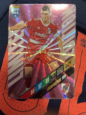 Panini FIFA 365 Lucas Beltrán kort - Samlarbild från Panini FIFA 365-serien med Lucas Beltrán i River Plates röda matchställ. Kortet har glittrig yta och visar spelarens stats. Perfekt för dig som gillar fotboll och samlarkort.