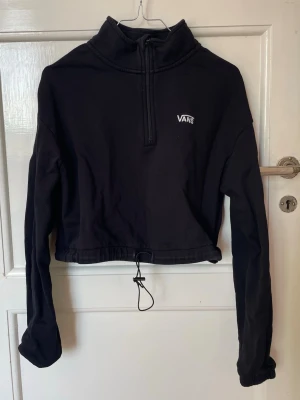 Cropped tröja från Vans - Svart, mjuk tjocktröja från Vans. Cropped modell som man kan dra åt i midjan. Half zip