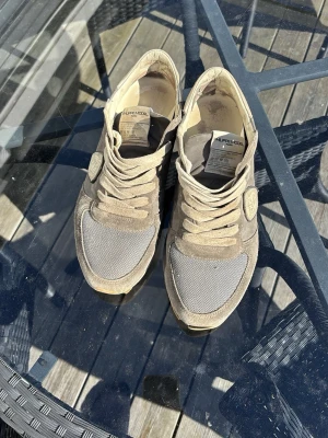 Beige sneakers från Philippe Model - Snygga sneakers från Philippe Model i beige mocka och mesh. Skorna har klassisk låg profil, beige snörning och detaljerad logotyp på sidan. Perfekta för dig som gillar stilrena och bekväma sneakers med en sportig touch.