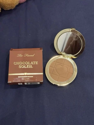Too Faced Chocolate Soleil Bronzer - Bronzer från Too Faced i nyansen Chocolate Soleil. Kommer i en rund, guldig dosa med spegel och ett pressat hjärtmönster i pudret. Färgen är matt, mediumbrun och ger en naturlig solkysst look. Förpackningen är brun med gulddetaljer. Endast testad, säljer pga köpte fel färg