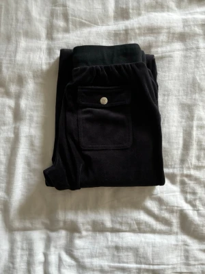 Svarta mjukisbyxor med raka ben - Säljer ett par svarta mjukisbyxor i mjukt velourmaterial. Byxorna har raka ben, resårmidja med dragsko och två fickor fram. Innebenslängd 69cm.  Perfekta för chill dagar hemma eller när du vill vara bekväm men ändå se snygg ut.