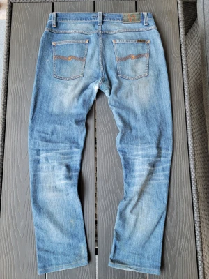 Ljusblå nudie jeans - Säljer ett par ljusblå nudie jeans. Jeansen har raka ben, klassiska fem fickor och kontrastsömmar. Materialet är denim i bomul. Perfekta för en avslappnad och trendig stil. Obs! De har tydliga tecken på slitningar(hål i ena knät och lagningar bid skrevet). Dock inget som syns vid användning