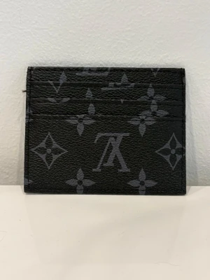Svart  kortfodral - Snyggt svart kortfodral  med klassiskt monogrammönster i grått. Fodralet har flera kortfack och är tillverkat i tåligt läder. Perfekt för dig som vill ha en stilren och exklusiv accessoar i fickan.