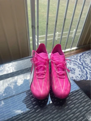 Rosa fotbollsskor från Puma - Säljer ett par snygga fotbollsskor från Puma i en riktigt skarp rosa färg med vita och svarta detaljer. Skorna har låg profil, snörning och en lätt ovandel som ger bra bollkontroll. Perfekta för dig som vill sticka ut på planen! Använda 2 gånger på konstgräs vilket förklarar svarta färgen på dom