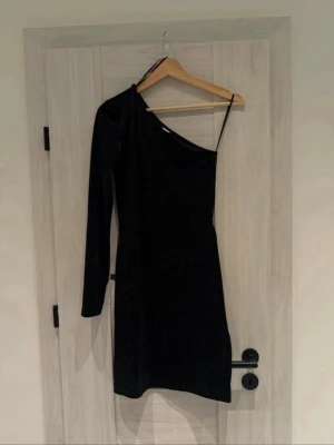 Elegant One-Shoulder Sammetsklänning från & Other Stories - Ge din garderob en touch av lyx med denna ursnygga svarta klänning! Den perfekta kombinationen av stilren elegans och en modern twist med sin asymmetriska design. Om klänningen: • Märke: & Other Stories (Stockholm Atelier). • Modell: One-shoulder med en lång ärm – skapar en fantastisk siluett! • Material: Mjuk och glansig krossad sammet som ger ett lyxigt djup. • Storlek: XS (EU 34). • Skick: Aldrig använt så helt ny • 🏠 Rök- och djurfritt hem. • ⚡  Fraktar inom 24h!