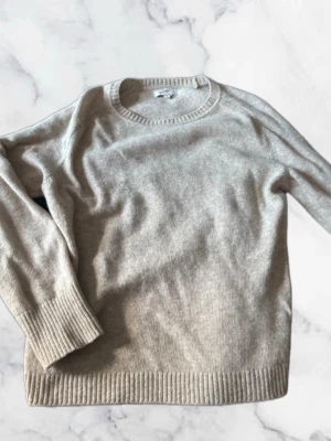 Beige Grandpa stickad tröja  - En stilren beige stickad tröja med rund halsringning och långa ärmar. Tröjan har breda ribbade muddar vid ärmslut och nederkant, vilket ger en snygg och klassisk look. Perfekt för lager-på-lager och enkel att matcha med olika outfits.