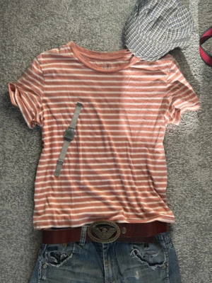 Slim fit randig t-shirt från GAP i bomull - Säljer min randig t-shirt från GAP i mjuk ekologisk bomull. T-shirten är korallrosa med vita ränder, har rund hals och korta ärmar. Perfekt för en avslappnad stil.