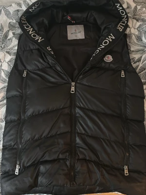 Moncler puffer vest - Snygg svart dunväst från Moncler med bra kvalitet o ganska bra skick med unik design allt är perfekt, bara att höger fickan har lite hål men går bra att sy annars helt perfekt och dunder vest! 