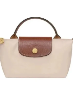 Beige handväska med brunt lock. Longchamp väska - Stilren beige handväska med brunt lock och handtag. Väskan har en klassisk, rektangulär form och stängs med ett guldfärgat trycklås. Materialet ser ut att vara en kombination av textil och läder, vilket ger en snygg kontrast mellan kropp och lock.