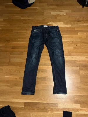 Mörkblå slim fit jeans från Replay - Säljer ett par mörkblå slim fit jeans från Replay med klassisk femficksmodell och snygga slitningar. Jeansen har låg midja och smal passform, perfekta till vardagslooken. Tillverkade i stretchigt denim för extra komfort.