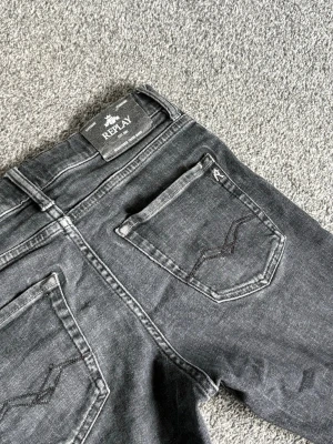 Svarta Replay jeans med raka ben - Säljer ett par svarta jeans från Replay med klassisk femficksmodell och raka ben. Jeansen har snygga detaljer på bakfickorna och Replay-logga både bak och fram. Perfekta för dig som gillar en stilren och tidlös look.