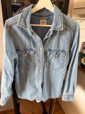 Ljusblå jeansskjorta Dallas XS - Säljer en ljusblå jeansskjorta från Dallas i storlek XS. Skjortan har klassisk krage, två bröstfickor med knappar och långa ärmar. Tillverkad i bomull och har tryckknappar framtill. Perfekt för en avslappnad och cool stil.