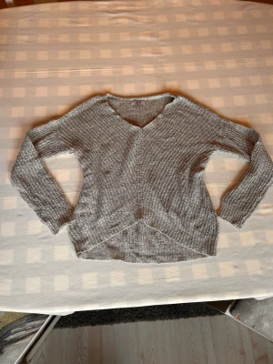 Grå stickad tröja med v-ringning - Säljer en grå stickad tröja med v-ringning och lång ärm. Perfekt för lager på lager och enkel att matcha med jeans eller kjol.
