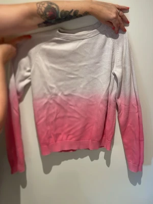 Vit och rosa ombre tröja - Säljer en snygg långärmad tröja med ombre-effekt från vitt upptill till rosa nedtill. Tröjan har rund halsringning och ribbade muddar vid ärmslut och nederkant. Perfekt för dig som gillar färg och vill sticka ut lite extra.