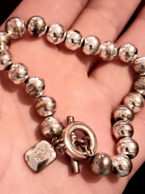 Silverfärgat ralph lauren  pärlarmband med toggle-lås - Säljer ett stilrent Ralph Lauren armband med stora, runda silverfärgade pärlor och ett snyggt toggle-lås ✨️ Armbandet passar perfekt för dig som gillar klassiska accessoarer med en modern twist. Lite slitet på vissa ställen (se bild) därav priset.