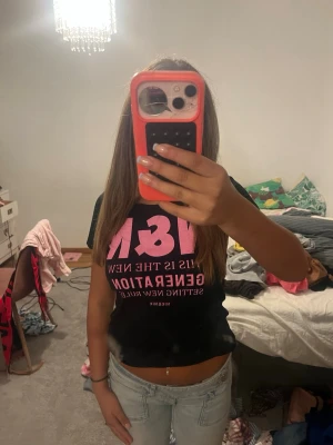 Svart t-shirt med rosa text - Snygg svart t-shirt med stor rosa text på bröstet och mindre text under. T-shirten har korta ärmar och en klassisk passform. Perfekt för dig som gillar statement-plagg och vill sticka ut lite extra.