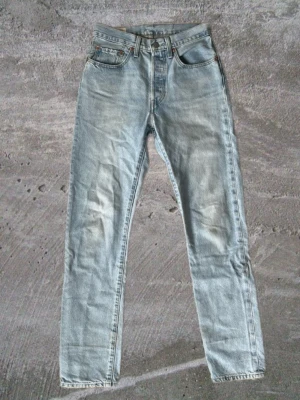 Levis 501 - Säljer ett par ljusblå Levis 501 👖. Jeansen har fem fickor, gylf med dragkedja och knapp samt tydliga slitningar för en vintagekänsla. Materialet är denim i bomull och de har en tidlös look. Mått 📏: Midjebredd: 35 Längd: 107