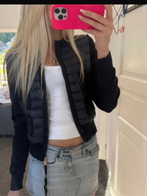 Moncler cardigan dam - Svart cardiganjacka från Moncler med quiltad framsida och tvåvägsdragkedja. Jackan har långa ärmar i stickat material och fyra fickor framtill. Perfekt för lager-på-lager och snygg till både jeans och kjol.