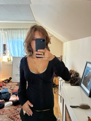 Svart långärmad topp - Snygg svart långärmad topp med djup v-ringning och figurnära passform. Toppen har en enkel design som framhäver siluetten och är perfekt för dig som gillar en stilren look. Materialet känns mjukt och stretchigt, vilket gör den bekväm att bära.
