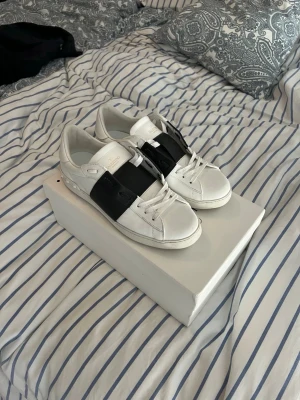 Valentino opens  - Snygga vita valentino opens med ett brett svart band över mitten. Skorna har klassisk låg profil och vita snören. Tillverkade i slätt läder med diskreta detaljer och en stilren look som passar till det mesta.