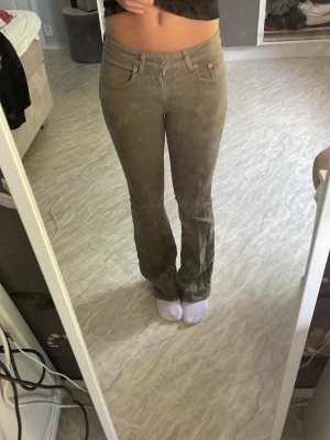 Beiga bootcut jeans med låg midja - Säljer ett par snygga gröna jeans med bootcut-modell och låg midja. Jeansen har klassiska fem fickor och stängs med dragkedja och knapp. Perfekta för dig som gillar en avslappnad men trendig stil.