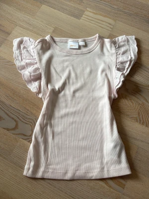 Ljusrosa topp med volangärmar Gina Tricot - Supersöt ljusrosa ribbad topp från Gina Tricot med volangprydda ärmar i spets. Perfekt för dig som vill ha en feminin och trendig look. Toppen är ärmlös med breda axelvolanger och har en mjuk, stretchig känsla.
