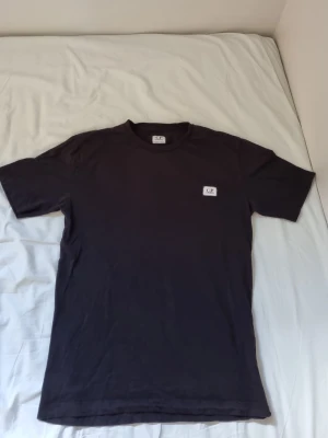 Svart t-shirt från C.P. Company - Snygg svart t-shirt från C.P. Company med rund hals och diskret logga på bröstet. Använd 2-3 gånger! Tillverkad i mjukt bomullstyg som känns skönt mot huden. Perfekt basplagg för en clean och stilren look.