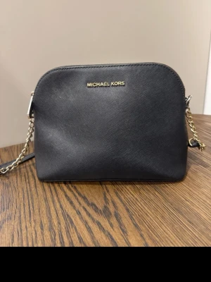 Svart axelväska från Michael Kors - Michael Kors väska i svart saffianoläder med guldfärgade detaljer. Klassisk och stilren modell som passar både till vardags och finare tillfällen.  Väskan är i fint begagnat skick och har förvarats väl. Justerbar axelrem samt rymlig insida med plats för det viktigaste.  ✨ Äkta Michael Kors 🖤 Svart saffianoläder ✨ Guldfärgade detaljer 👜 Justerbar axelrem ✨ Fint begagnat skick