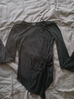 Svart omlottopp från Gina Tricot - Snygg svart omlottopp från Gina Tricot i mjukt material. Toppen har långa ärmar och en knytning i sidan som ger en cool twist till looken. Perfekt att styla med jeans eller kjol för en trendig outfit.