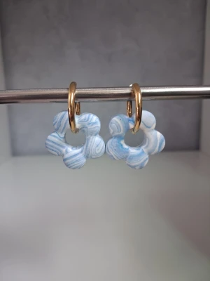 Blåvita blommiga örhängen jesmonite  - Unika örhängen med blommor i blåvitt mönster och guldfärgade ringar. Blommorna har en swirl-effekt och är tillverkade i materialet jesmonite, Perfekt accessoar för att addera färg och personlighet till din stil. Öronkroken är tillverkad i rostfritt stål. Blomman är 2.5cm stor 