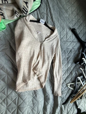 Beige kofta från Sincerely Lace - Beige kofta från Sincerely Lace med diskret mönster och en knapp framtill. Koftan har lång ärm och en mjuk, tunn stickning som passar perfekt till lager-på-lager. Enkel och stilren design som är lätt att matcha.
