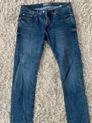 Mörkblå slim fit jeans - Snygga mörkblå slim fit jeans med klassisk femficksdesign och normal midja. Jeansen har en lätt tvättad look och raka ben. Perfekta för en avslappnad och trendig stil. Materialet är troligtvis bomull med lite stretch för extra komfort.