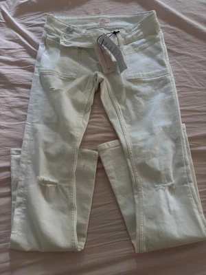 Vita jeans - Säljer ett par vita jeans med snygga slitningar på benen och broderade detaljer på bakfickorna. Bootcut och low waist.