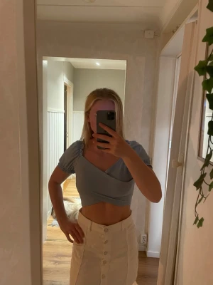Ljusblå och grön croppad omlottopp - Säljer två toppar med omlottdesign och puffiga korta ärmar. Toppen har en snygg v-ringning och sitter tight över kroppen. Perfekt för dig som vill ha en modern och stilren look.