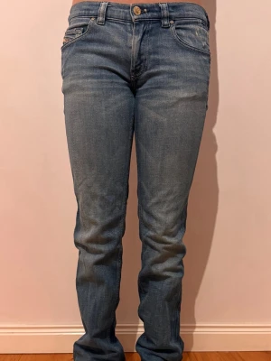 Blå vintage jeans med låg midja från Diesel - klassiska blå vintage jeans med rak passform och låg midja. Jeansen har fem fickor, bälteshällor och stängs med knapp och dragkedja. Materialet är mjukt denim i bomull och färgen är ljusblå med lätt slitning. Vintage. Diesel. Midjemått 37cm, ben innerlängd 86cm. W28 L32