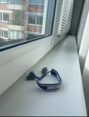 Blått tygarmband med text - Säljer ett blått tygarmband med vita detaljer och texten 'CHRISTIAN' broderad på bandet. Armbandet har tofsar i ändarna och justerbar knytning. Perfekt accessoar för en personlig stil. Pris kan diskuteras 
