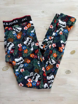 Färgglada kalsonger med dödskallar - Säljer ett par kalsonger från JACK & JONES med svart botten och färgglatt mönster av dödskallar, blommor och blad i orange, grönt, blått och vitt. Resårmidja med logga. Perfekta för dig som gillar unika och vågade prints.