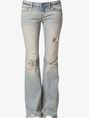 Ljusblå bootcut jeans med slitningar - Snygga ljusblå bootcut jeans med slitningar och hål på knäna och låret. Jeansen har fem fickor, låg midja och råa kanter nertill. Perfekta för en avslappnad och trendig look. Materialet är klassisk denim i bomull. 
