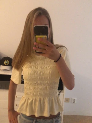 Gul smockad topp med volang - Söt ljusgul topp med smockad midja och volang nedtill. Toppen har korta ärmar och en figurnära passform.🤍