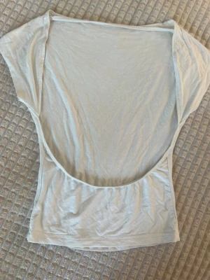 Vit topp med öppen rygg - Säljer en vit topp i mjukt material med en riktigt djup öppen rygg. Toppen är ärmlös och har en enkel, clean look som passar perfekt till jeans eller kjol. Lätt och luftig, perfekt för varma dagar eller lager på lager.