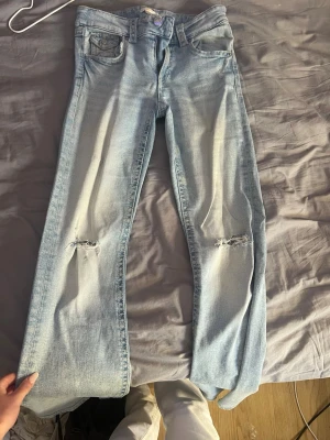 Ljusblå slitna jeans från Gina Tricot - snygga lågmidjade bootcut jeans från gina med slitningar på knäna har samt en litet slitning på bakfickan som man kan se på sista bilden det syns inte när byxorna är på annars är det superlätt att sy ihop då de inte ens är ett hål utan mer lite lösa trådar