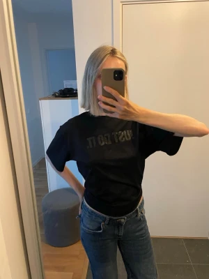 Svart träningströja från Nike med knytning och tryck  - Säljer en svart träningströja från Nike i storlek S med texten 'JUST DO IT' tryckt på bröstet. T-shirten har korta ärmar och en knytning i ryggen. 50 kr!