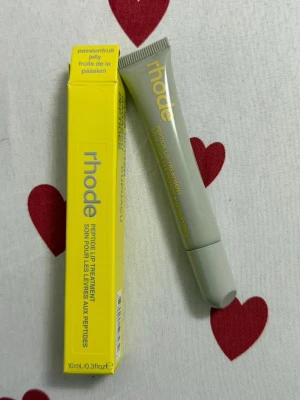 Rhode Peptide Lip Treatment Passionfruit - Rhode Peptide Lip Treatment i smaken Passionfruit Jelly. Läppbalsamet kommer i en stilren, ljusgrå tub med gul text och tillhörande gul förpackning. Innehåller 10 ml och är perfekt för att återfukta och vårda läpparna med peptider.