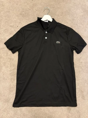 🖤 Lacoste Polo – Black Edition | Premium & Tidlös - En ikonisk Lacoste-piké i stilren svart färg – ett plagg som aldrig går ur mode. Perfekt för dig som vill ha en ren och exklusiv look, oavsett om det är till vardags eller en mer uppklädd outfit.  ✨ Detaljer • Klassisk broderad Lacoste-logga • Djupsvart färg som är lätt att matcha • Bekväm passform i hög kvalitet • Mycket fint skick – redo att användas direkt