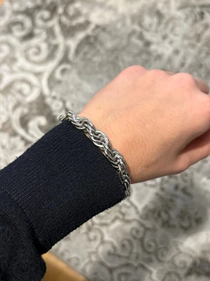 Tjockt flätat silverplaterad armband - Säljer ett stilrent armband i tjock, flätad kedja med silverfärgad finish. Armbandet har en robust karbinhake och passar perfekt för dig som gillar en clean och modern look. Materialet är metall och designen är chunky och trendig. Den är 10 mm tjock.