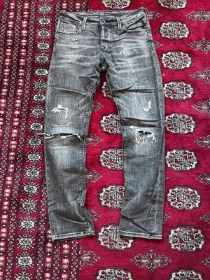 Grå slitna jeans med slitningar - Säljer ett par grå Diesel jeans med slitningar och hål på knäna. Jeansen har fem fickor, normal midja och smal passform. Materialet är klassisk denim i bomull med en cool tvättad look och distressed detaljer.