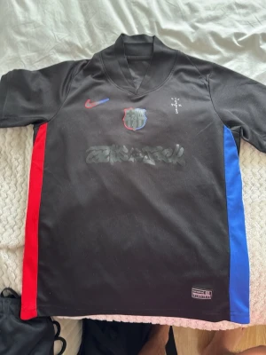 Svart FC Barcelona matchtröja Nike - Säljer en svart FC Barcelona matchtröja från Nike med röda och blå detaljer på sidorna. Tröjan har klubbmärke och Nike-logga på bröstet samt spelarnamn 'Raphinha' och nummer 11 på ryggen. Tillverkad i lätt och ventilerande material, perfekt för fotboll.